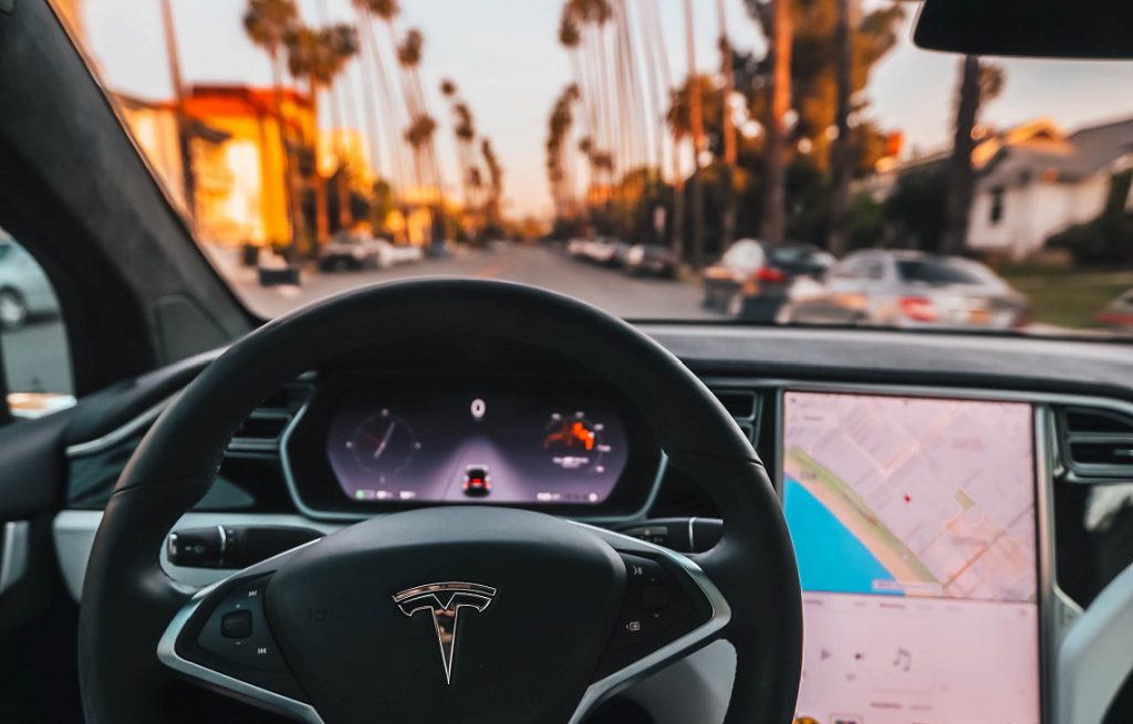 Tesla steering wheel and dashboard on a street with palm trees.