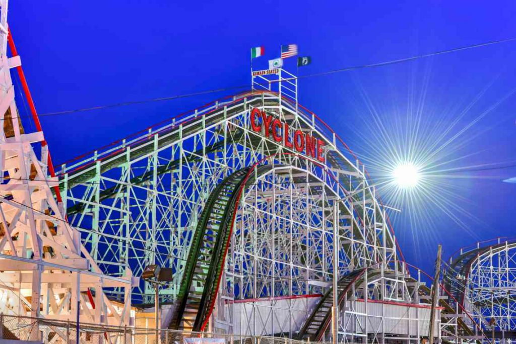 Red and white wooden rollercoaster with sun in the background.