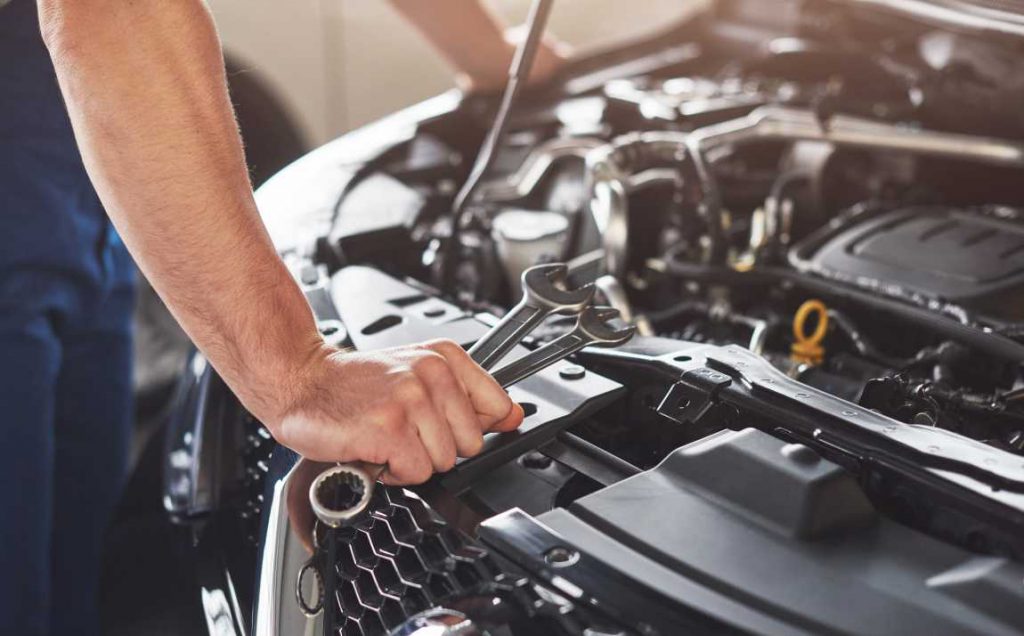 Man with wrenches in hand looking at car with the hood up