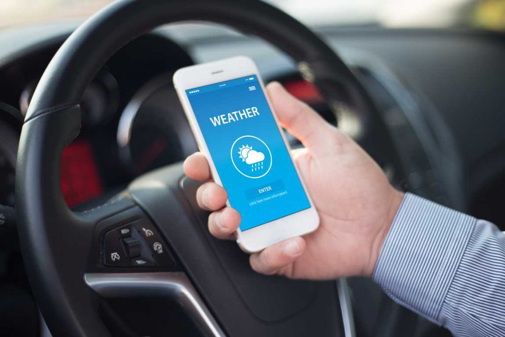 Man holding a phone with a weather app behind the steering wheel