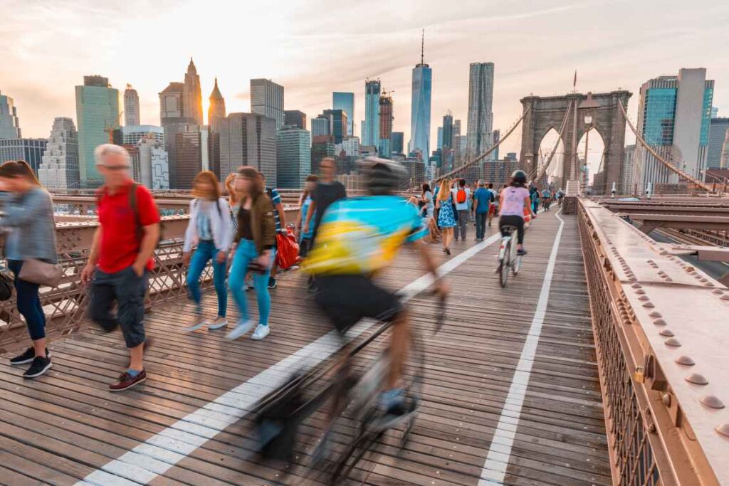 Cyclists riding across Brooklyn Bridge toward Manhattan with pedestrians