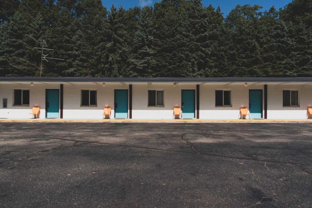 White motel with teal doors in front of evergreen trees