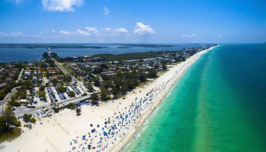 long stretch of white beach with many umbrellas on turquoise water from above