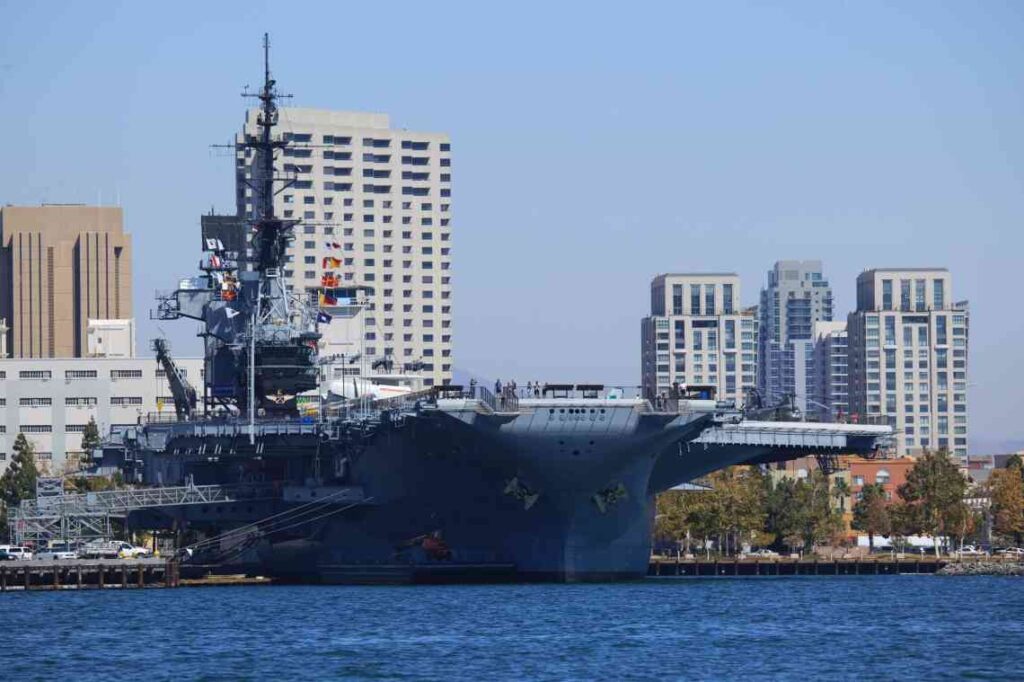 Large gray USS Midway aircraft carrier with San Diego skyline in the back