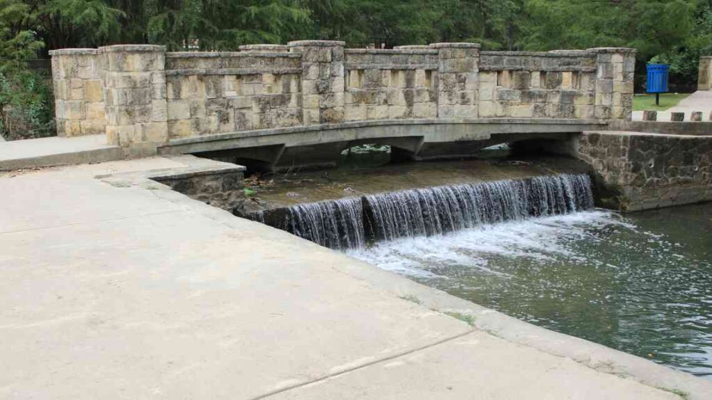 Old stone bridge over small waterfall in a park