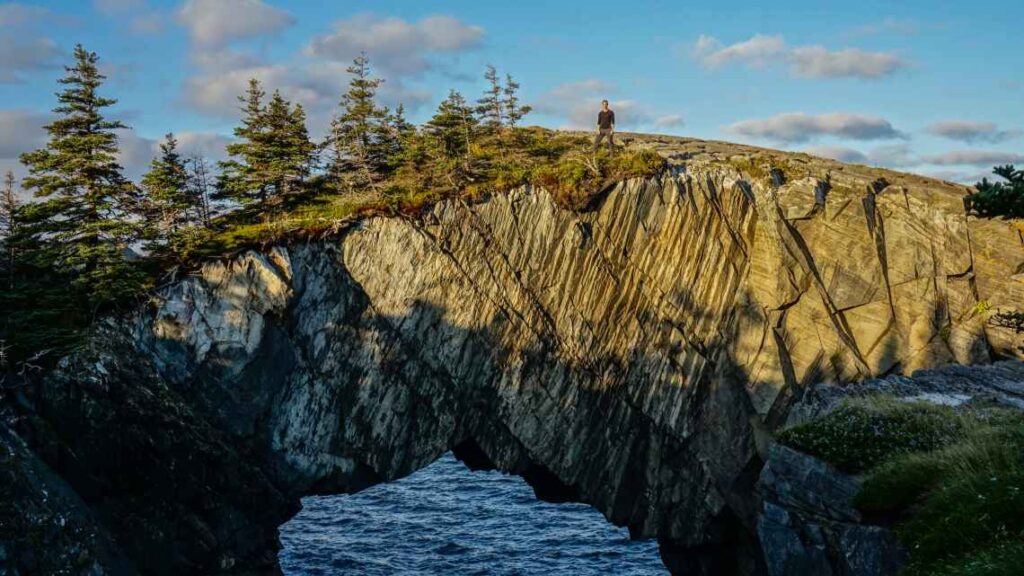 Arched rock formation over the water with hiker standing on top