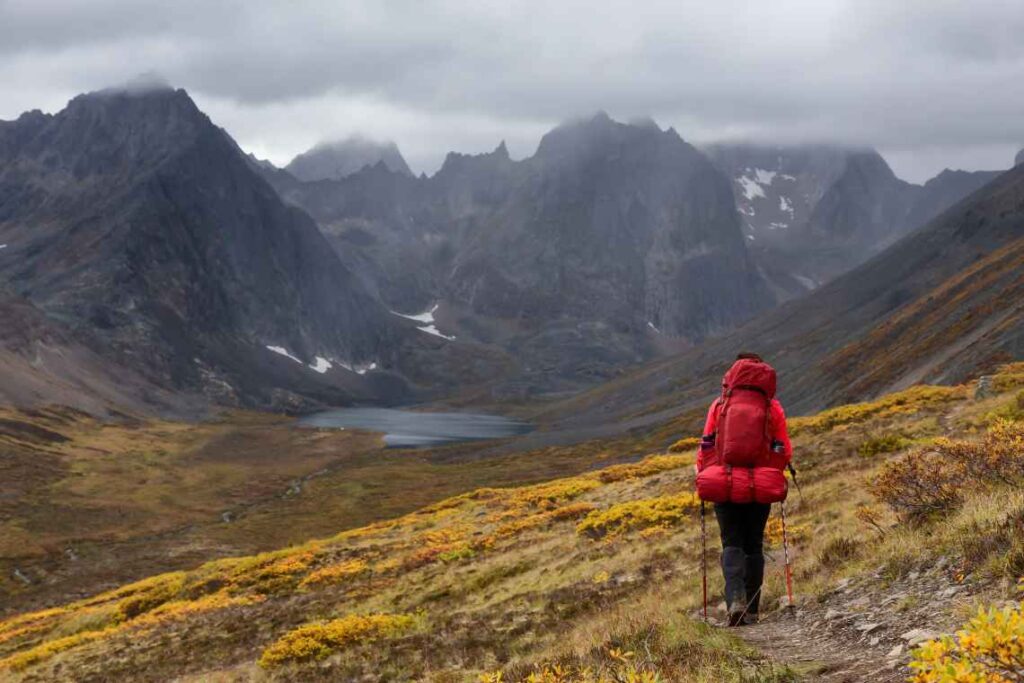 Hiker with red backpack on trail with lake and mountains in background