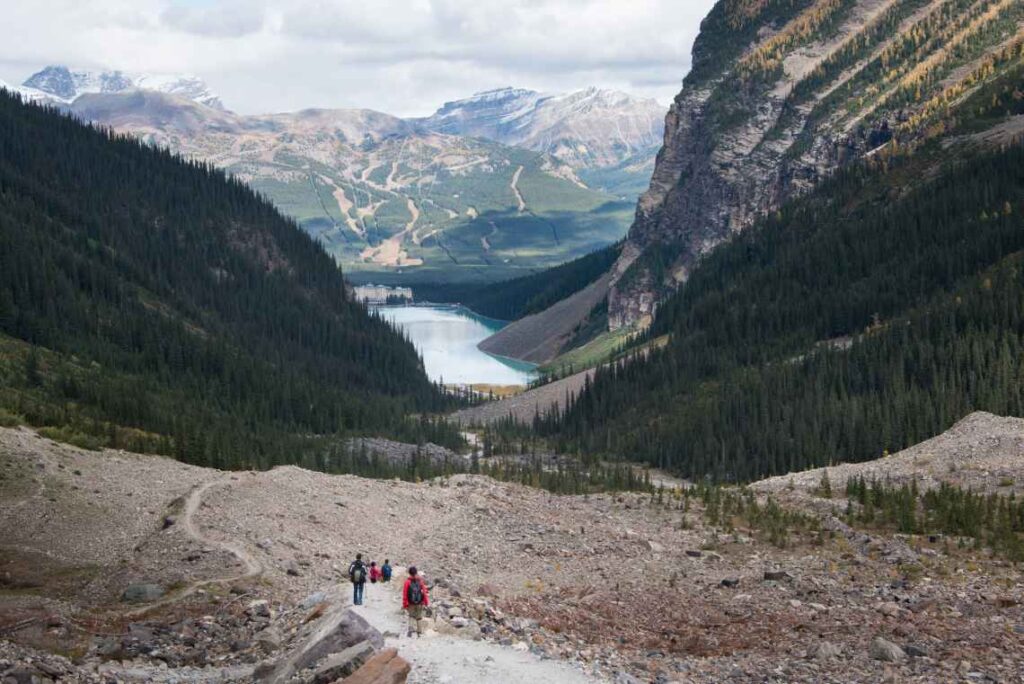 hikers on a dirt hiking trail above an alpine lake amid mountains