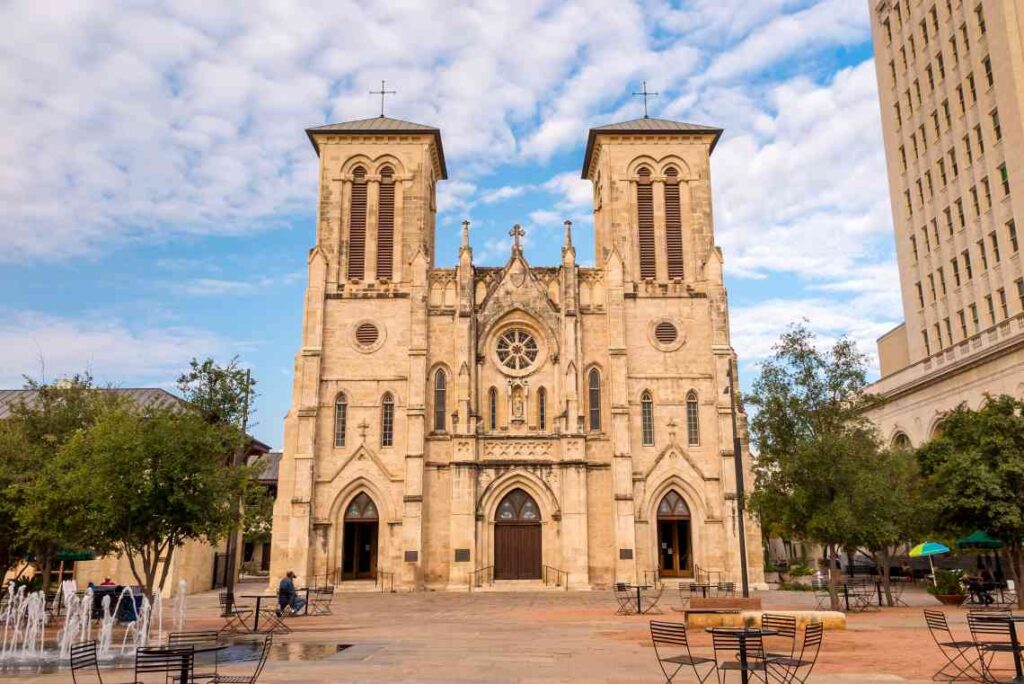The stone exterior of San Fernando Cathedral in front of a plaza with tables and chairs
