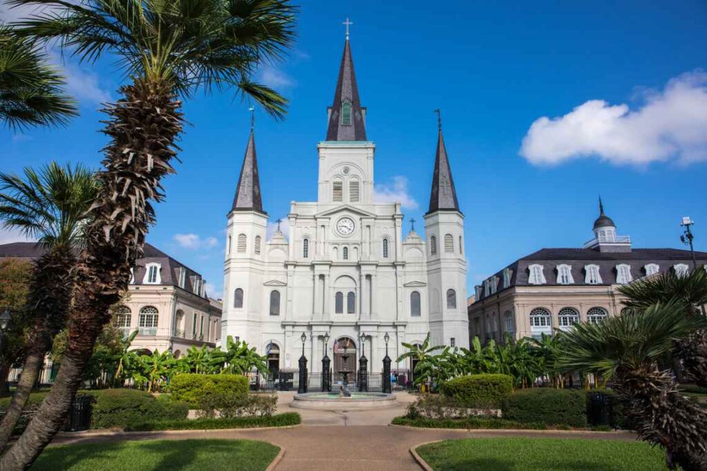 White exterior of a cathedral with 3 black spires with palm trees