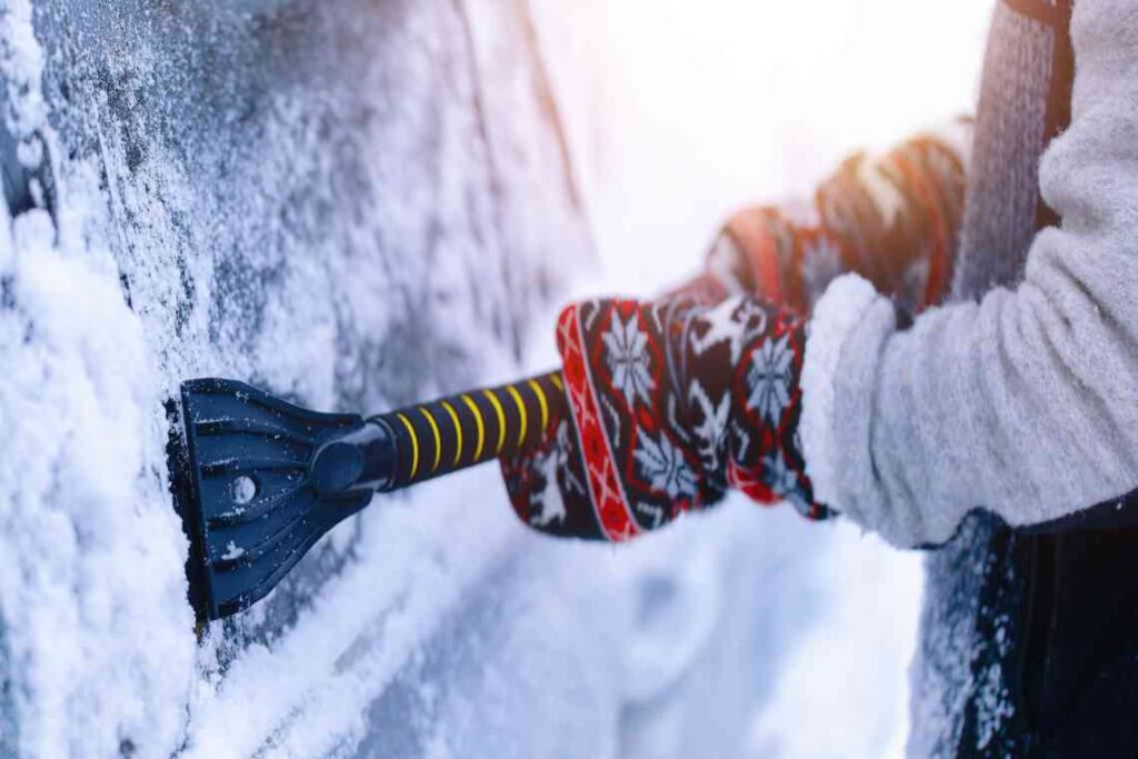 person wearing mitten scraping ice off car window