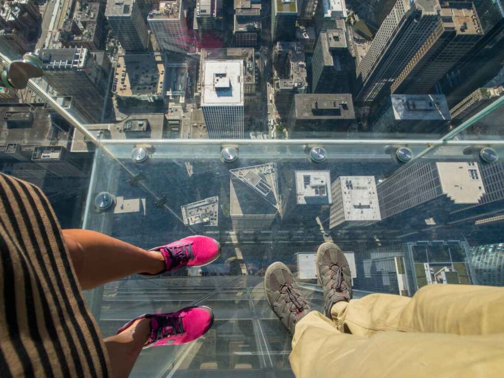 tourists standing in glass box above skyscrapers in chicago