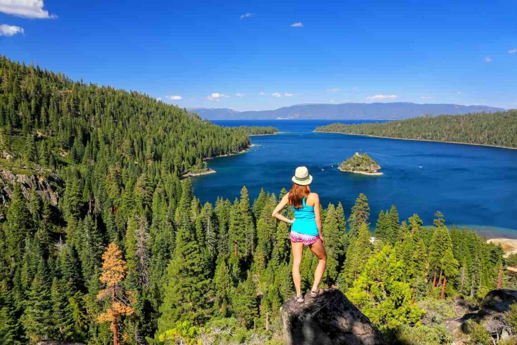 woman standing on a rock amid pine trees above lake tahoe