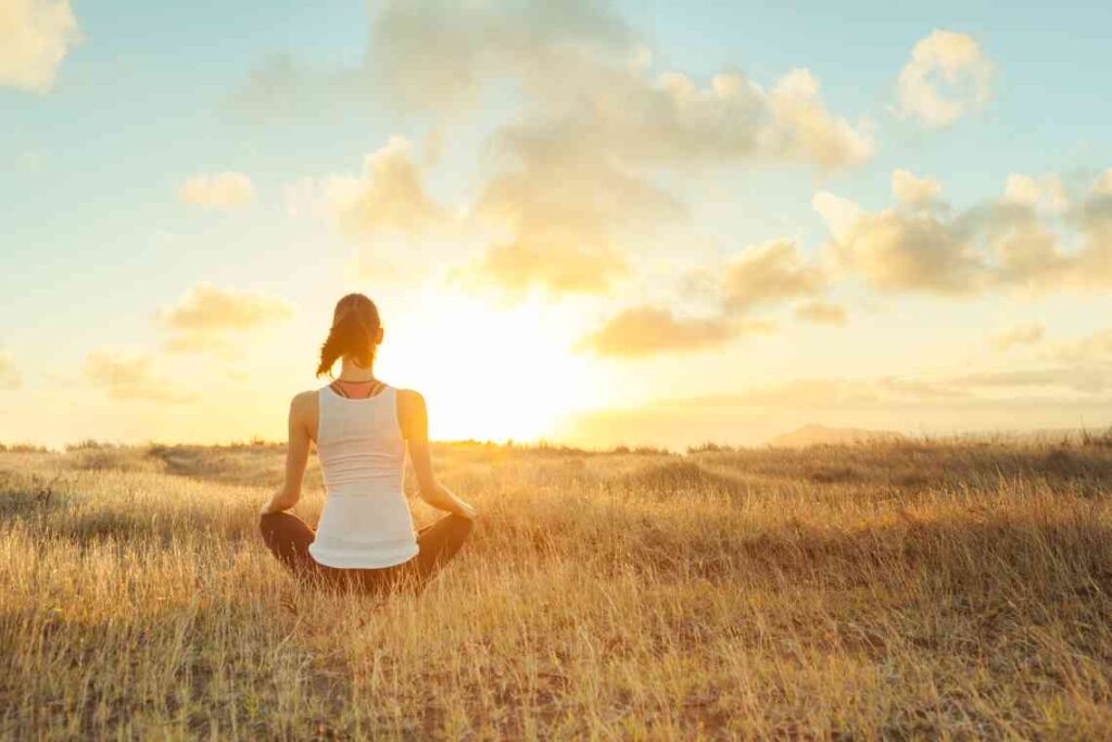 woman meditating in a field at sunset