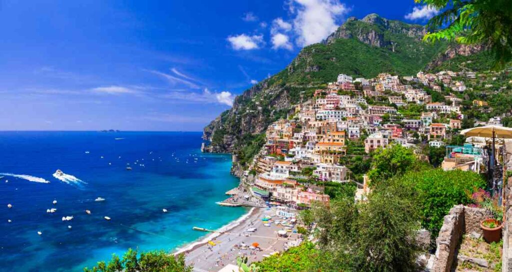 houses rising up the hill from a beach and blue-green water in Positano
