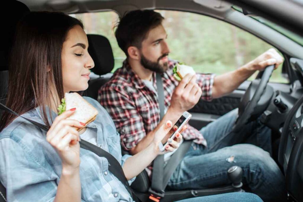 Man and woman sitting in car eating sandwiches