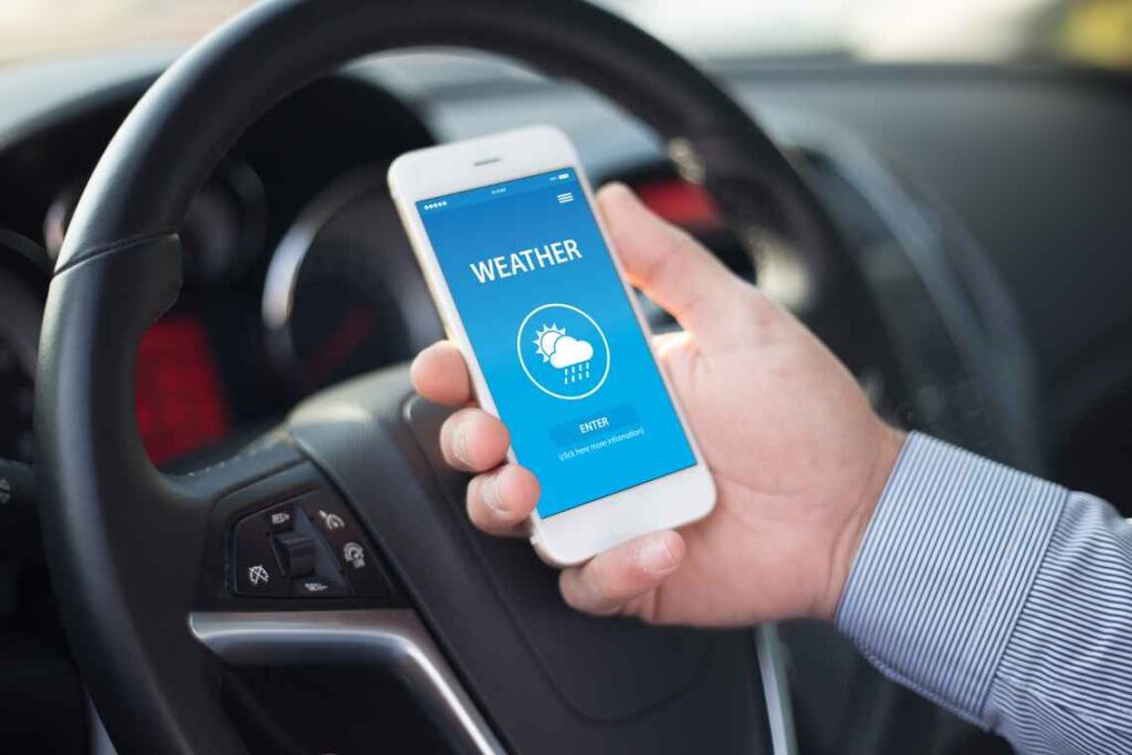 weather app on smartphone screen held in front of steering wheel