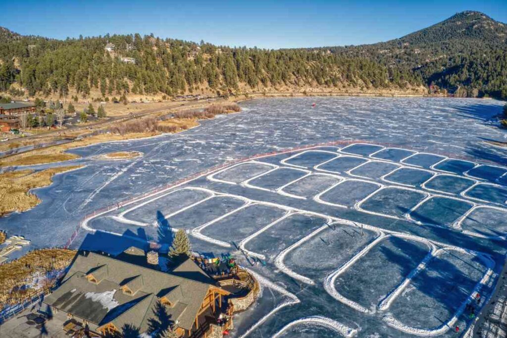 rectangles of ice skating rinks on a frozen lake surrounded by evergreen trees on hills and a large cabin home