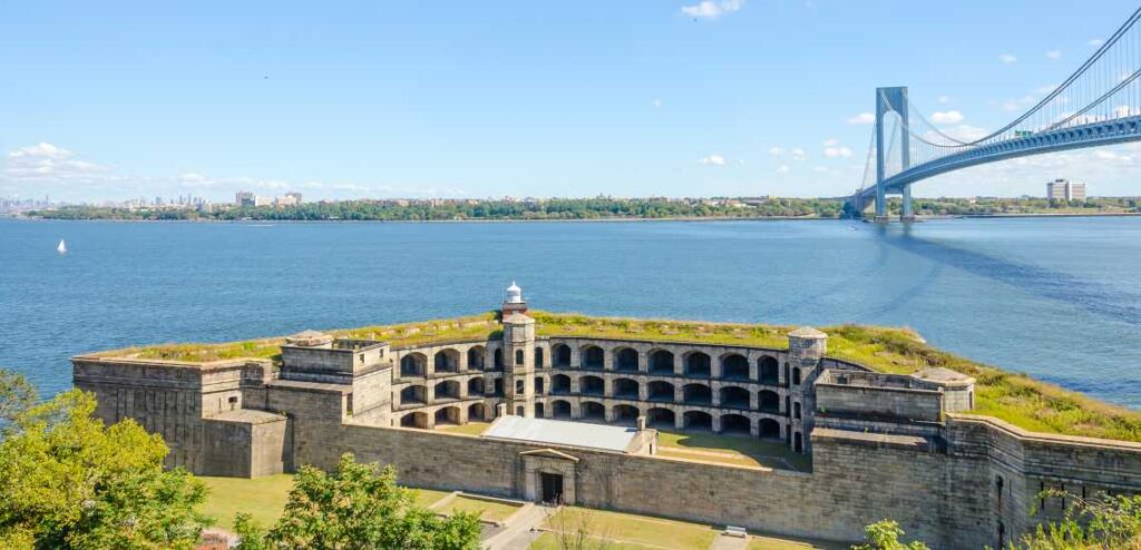 abandoned fort wadsworth with grass growing on top and blue suspension bridge above and water behind