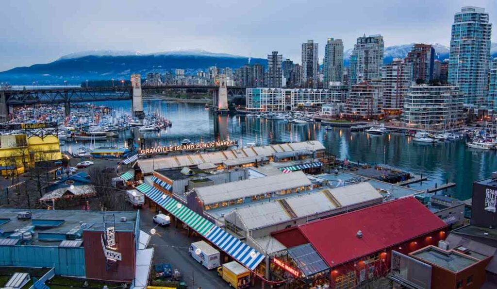 buildings on granville island, including the public market, from above with vancouver skyline and harbor in the background