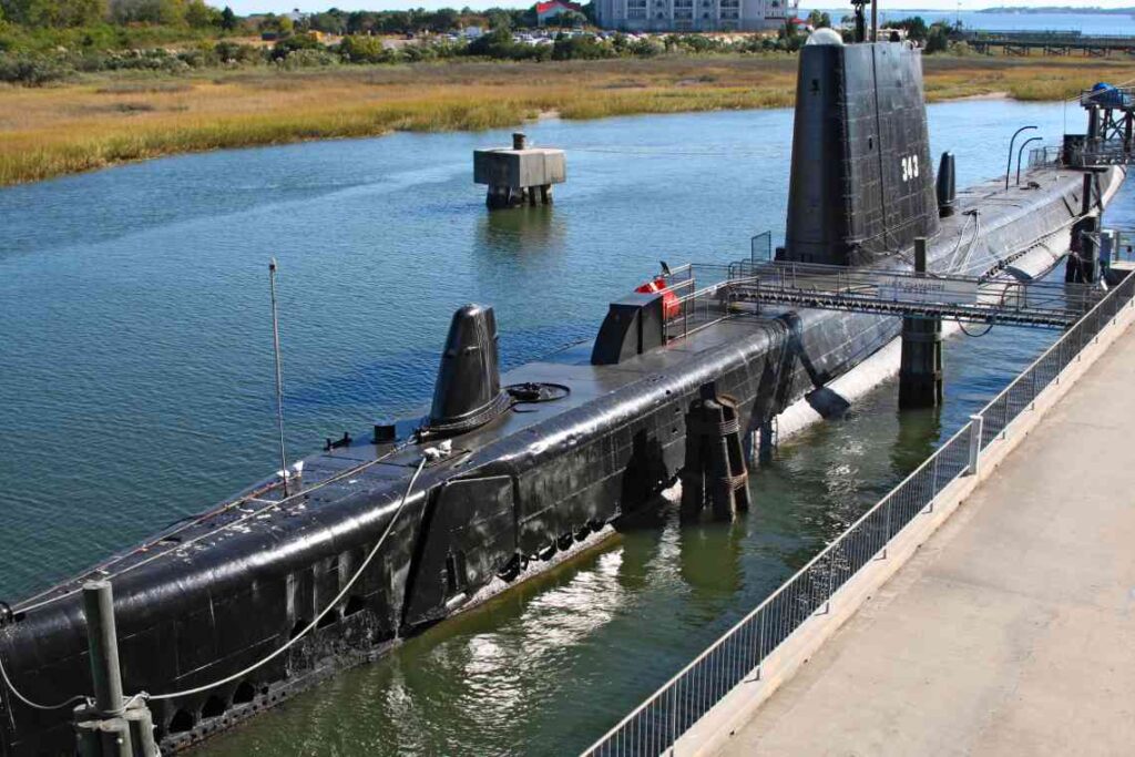 long black submarine docked above the water with a bridge leading to the opening