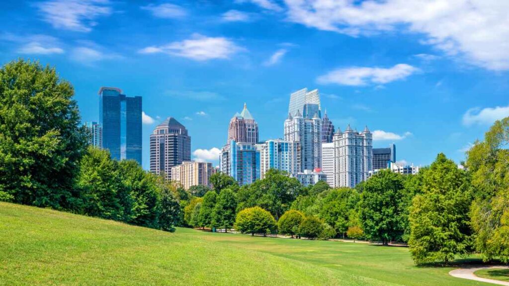green grass and trees in piedmont park with the midtown atlanta skyline in the background