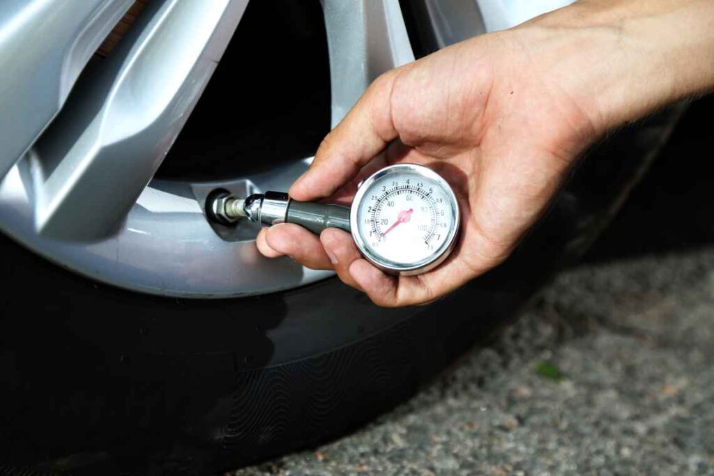 hand holding tire pressure gauge attached to car tire