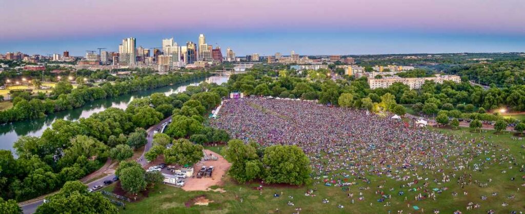 Large crowd in front of a stage in a park with Austin skyline and river in the background