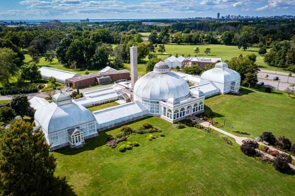 white domed greenhouse sitting on gree lawn with trees and pathways with bushes around it