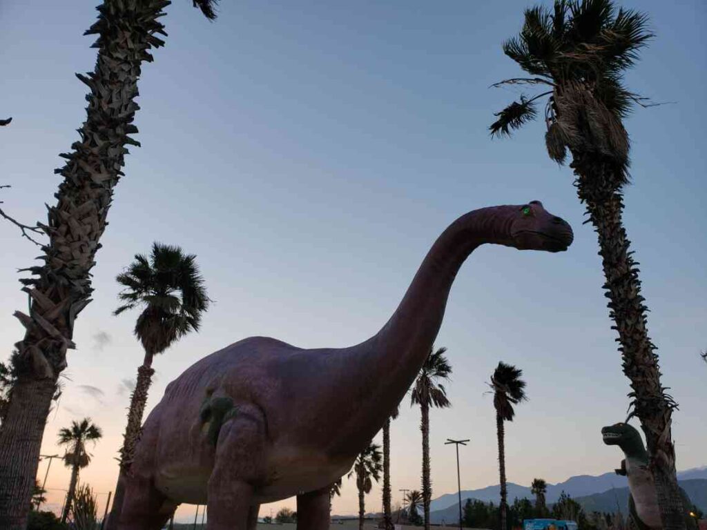 large dinosaur statue amid palm trees at dusk