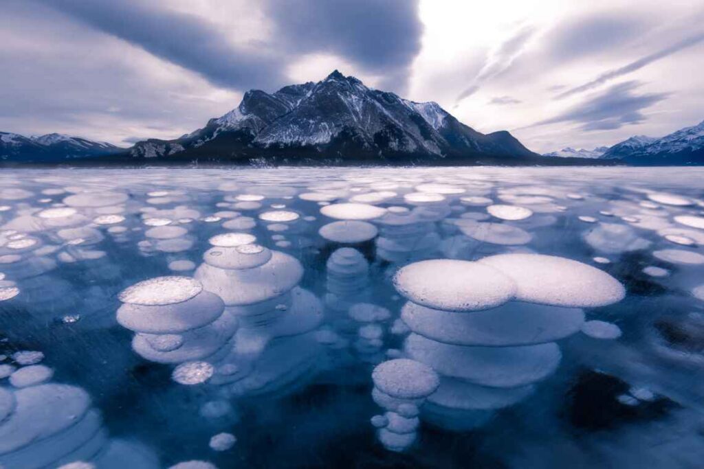 Black and white photo of air bubbles trapped in frozen Abraham Lake with a mountain in the background.