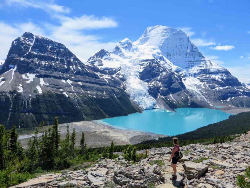 a hiker standing in front of bright blue berg lake with mount robson glacier in the background