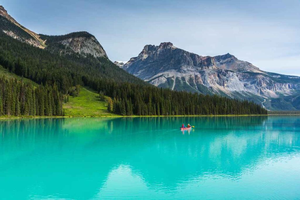 people in a red canoe rowing on turquoise Emerald Lake with mountains and forest in the background