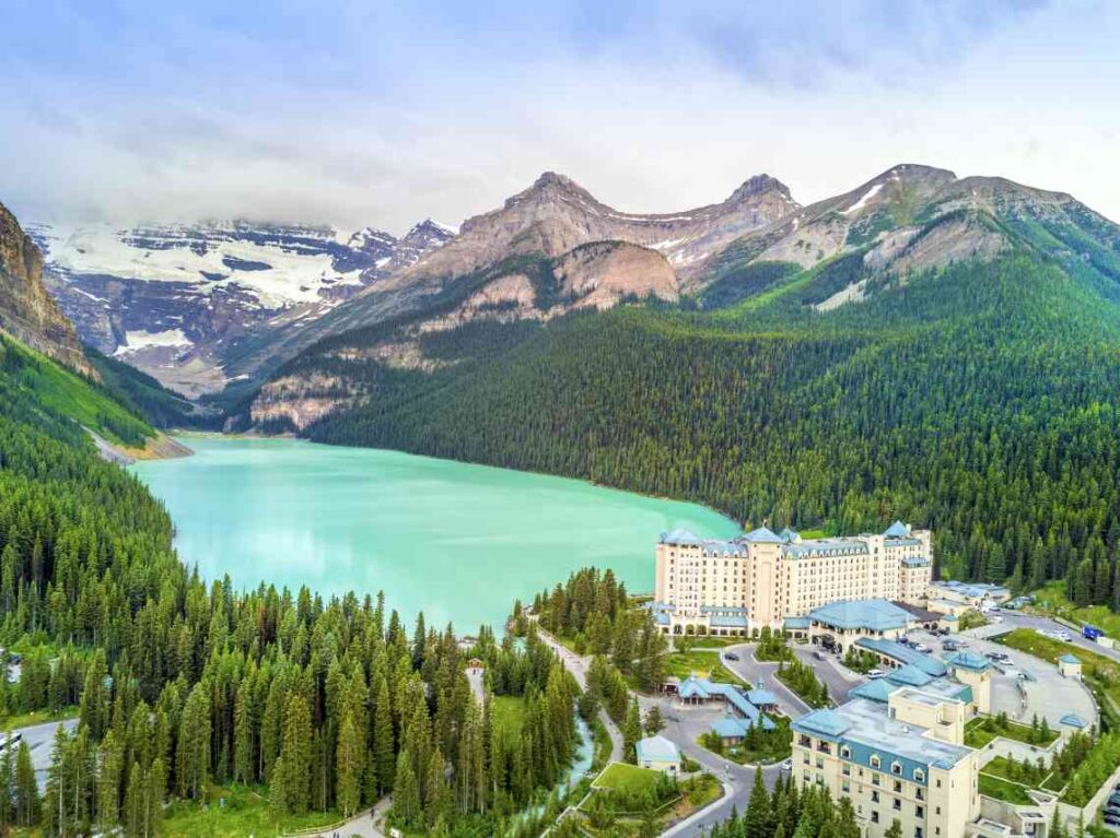 green lake louise from above, with a hotel, mountains and forests on the shore of the lake