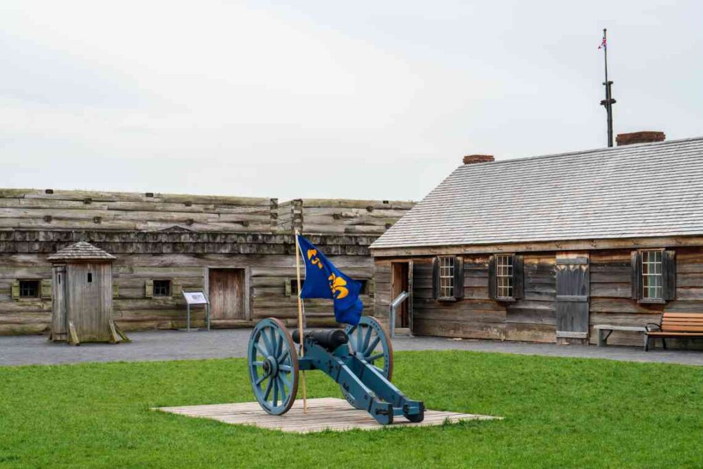 old wooden buildings with blue cannon with blue and yellow flag flying on it