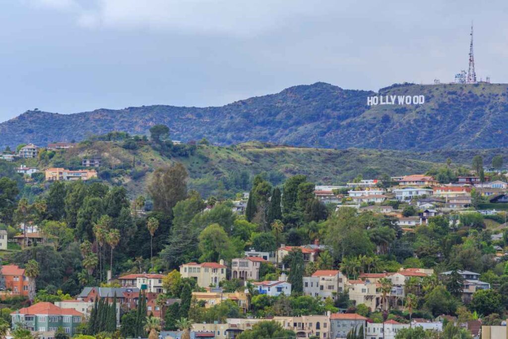 a far away view of the white hollywood sign on a hill, with houses in the foreground