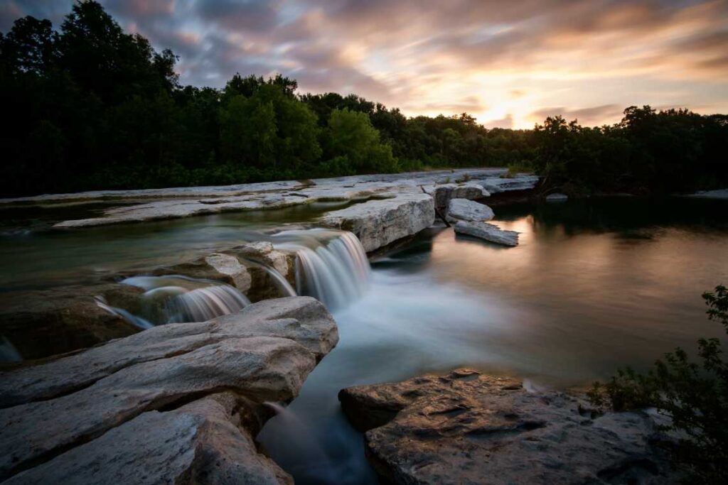 small waterfalls going over rocks in the river below at sunrise