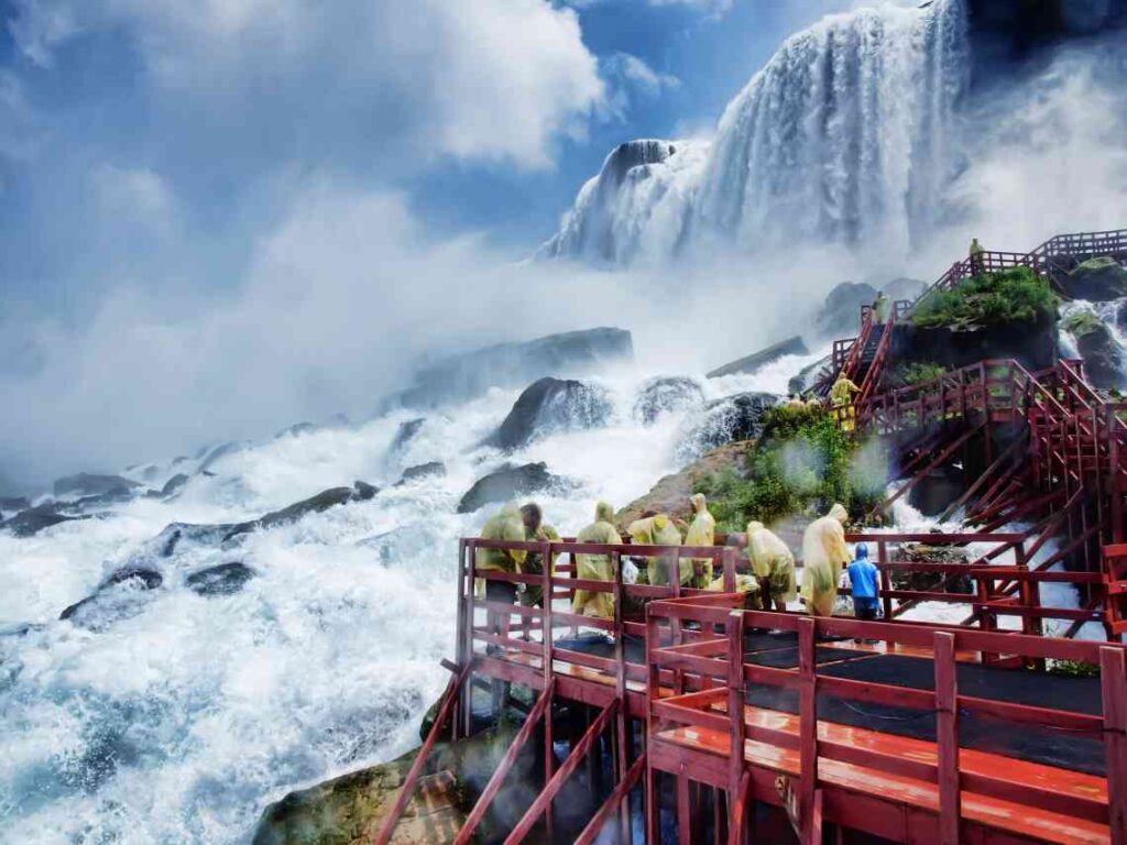 people in yellow ponchos on wooden red walkway below niagara falls