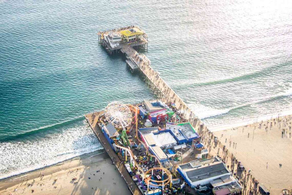 drone view of santa monica pier going in to the green pacific ocean with people on the beach on each side