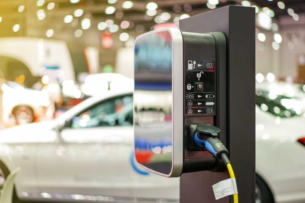 electric car charger with cable coming out of it and white 2-door car in the background