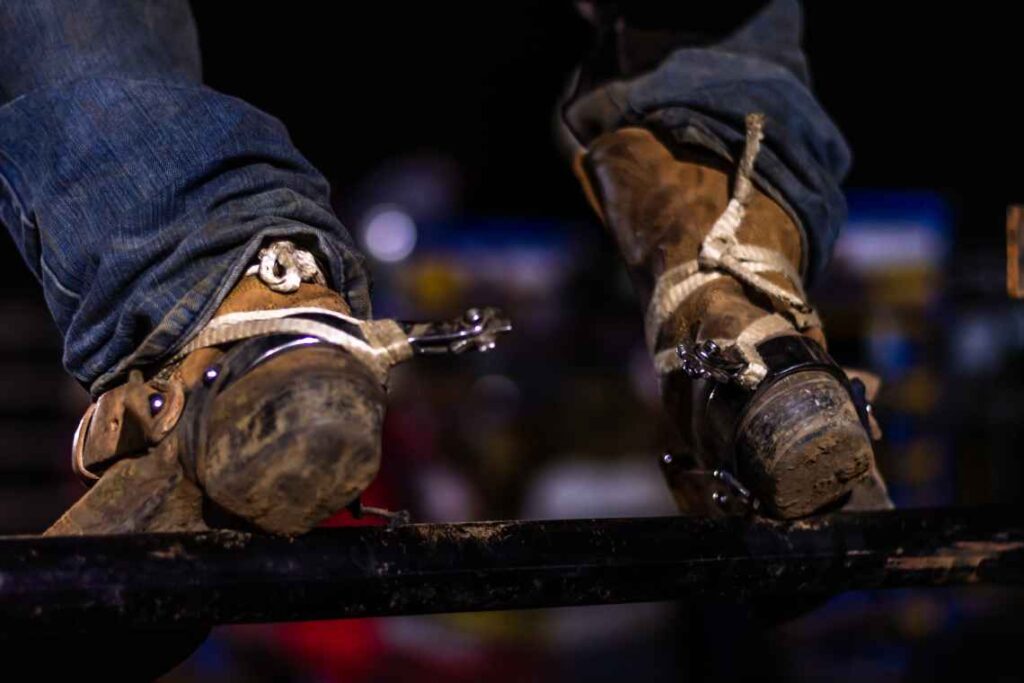 close up of muddy cowboy boots with spurs sitting on a fence rail
