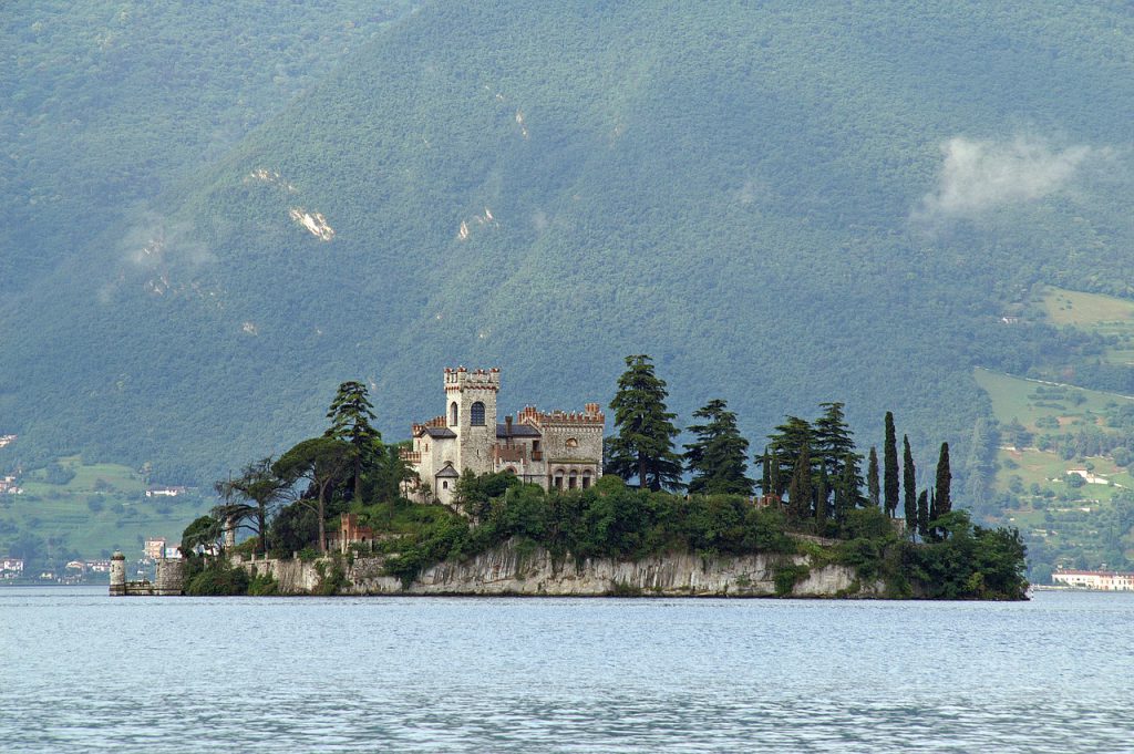 an island with green pine trees and a castle in the middle of Lake Iseo