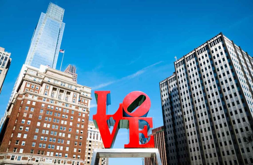 Red love sign with tall buildings in the background against blue sky