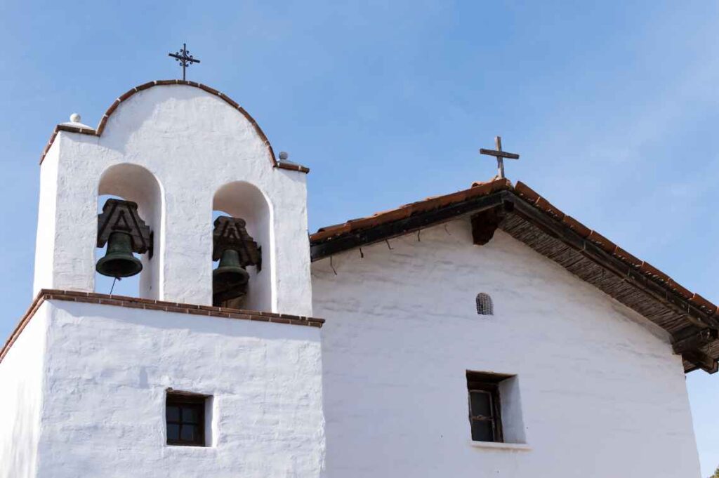 white spanish-style building with bell tower and a cross against blue sky