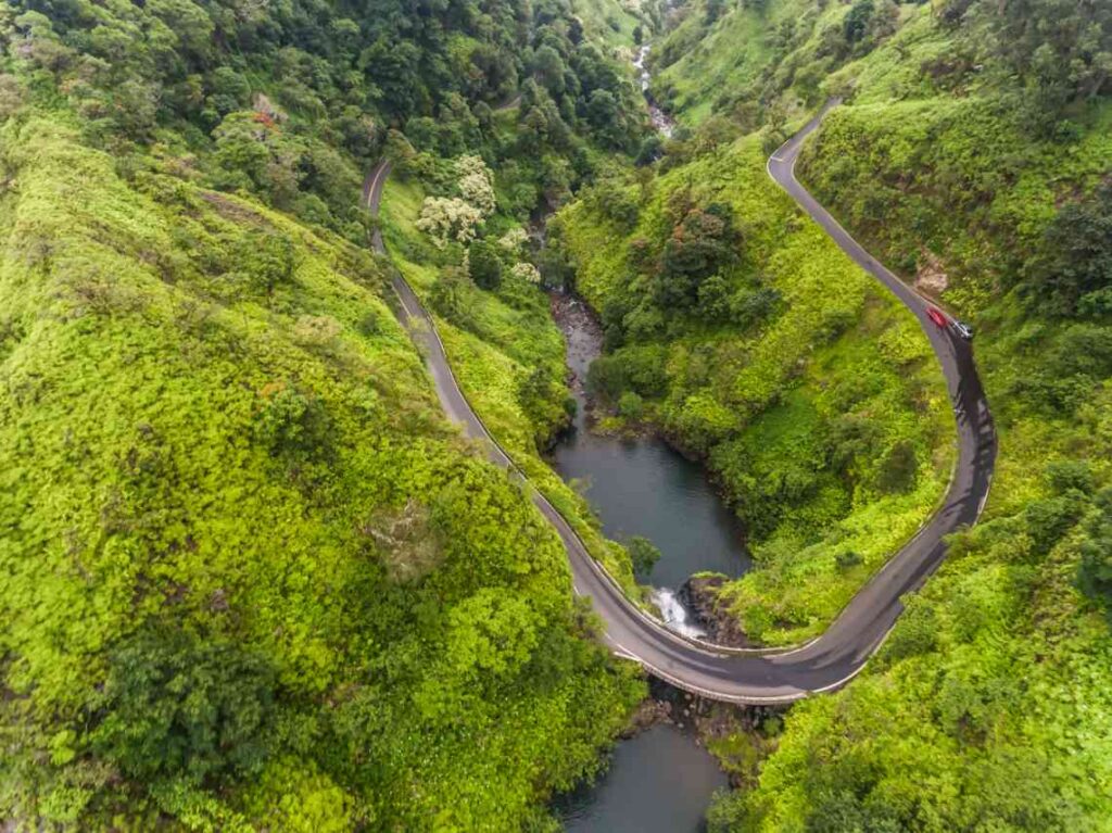 a portion of the road to hana snaking through green vegetation and hills with a river