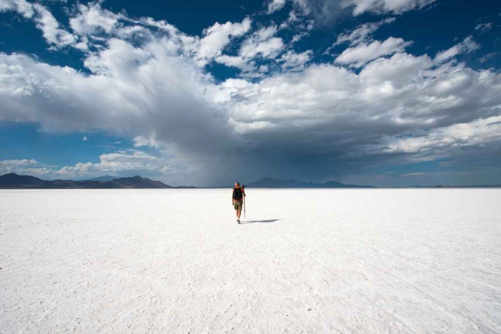 hiker with a pole on the white Bonneville salt flats with clouds and blue sky