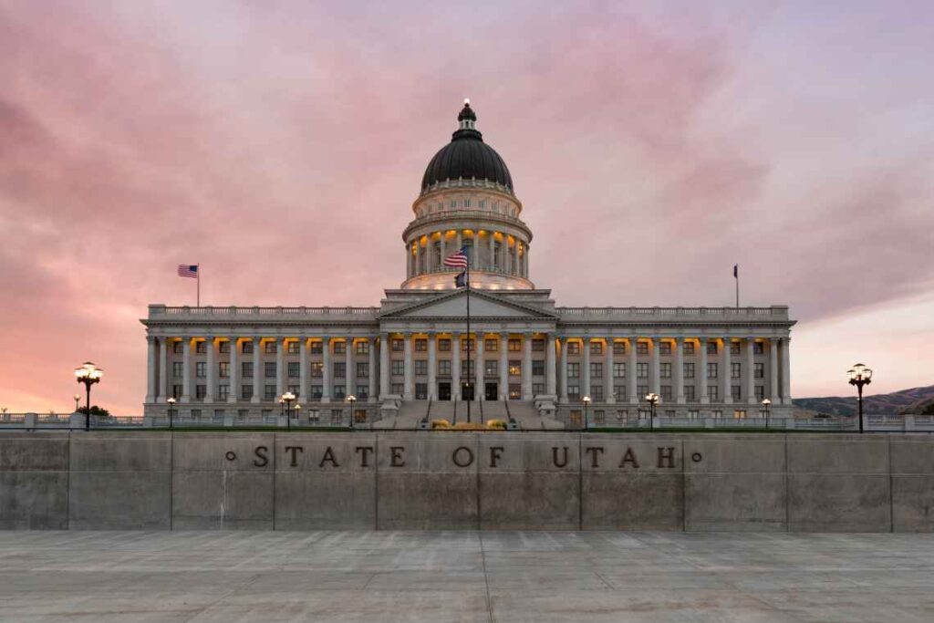 utah state capitol building with "state of utah" in front of it at sunset with purple clouds