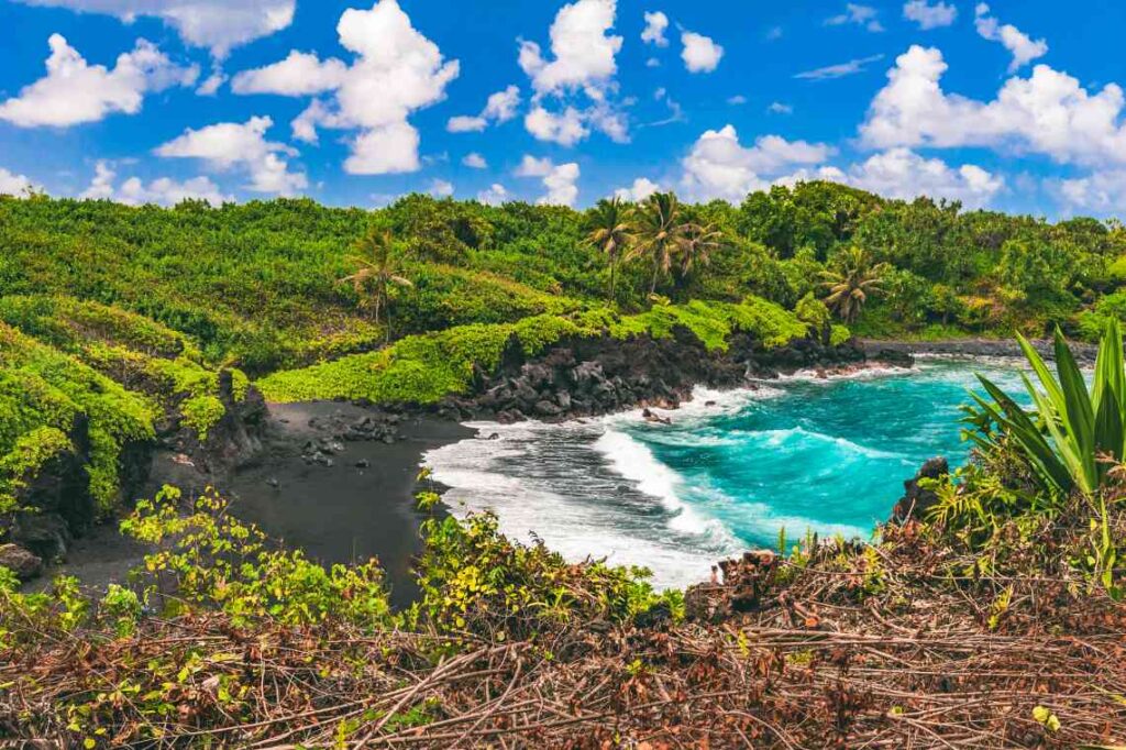 black sand beach on wai'anapanapa state park with turquoise water and lush greenery