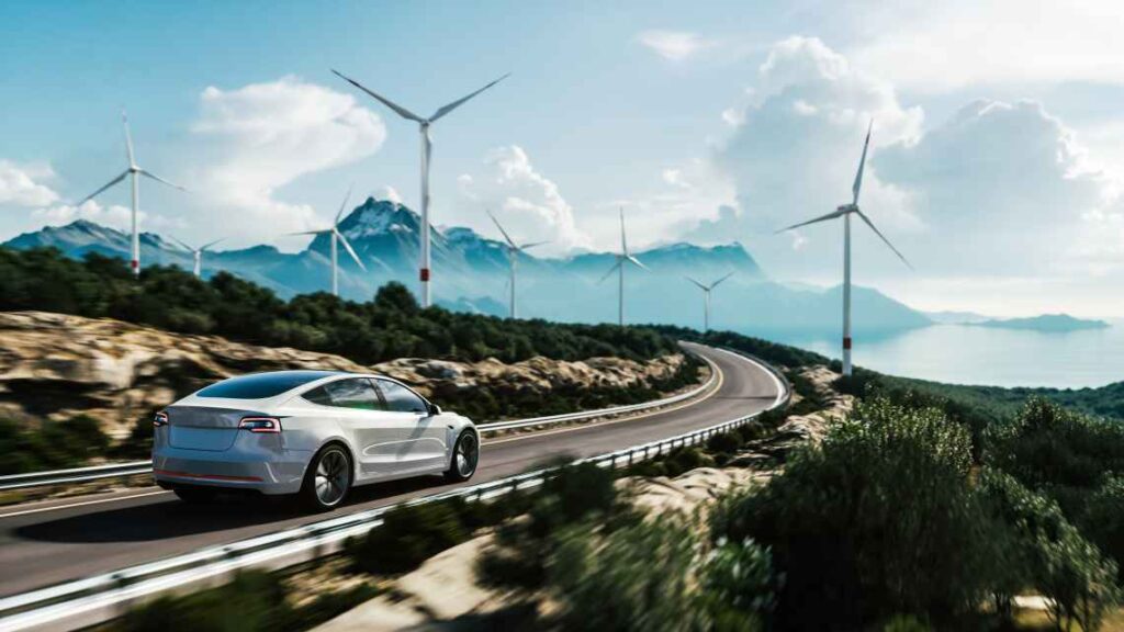 white Tesla driving down a highway with mountains and wind turbines