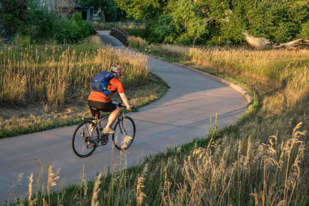 Man in shorts and a T-shirt wearing a backpack riding on a paved bike trail in fort collins colorado 